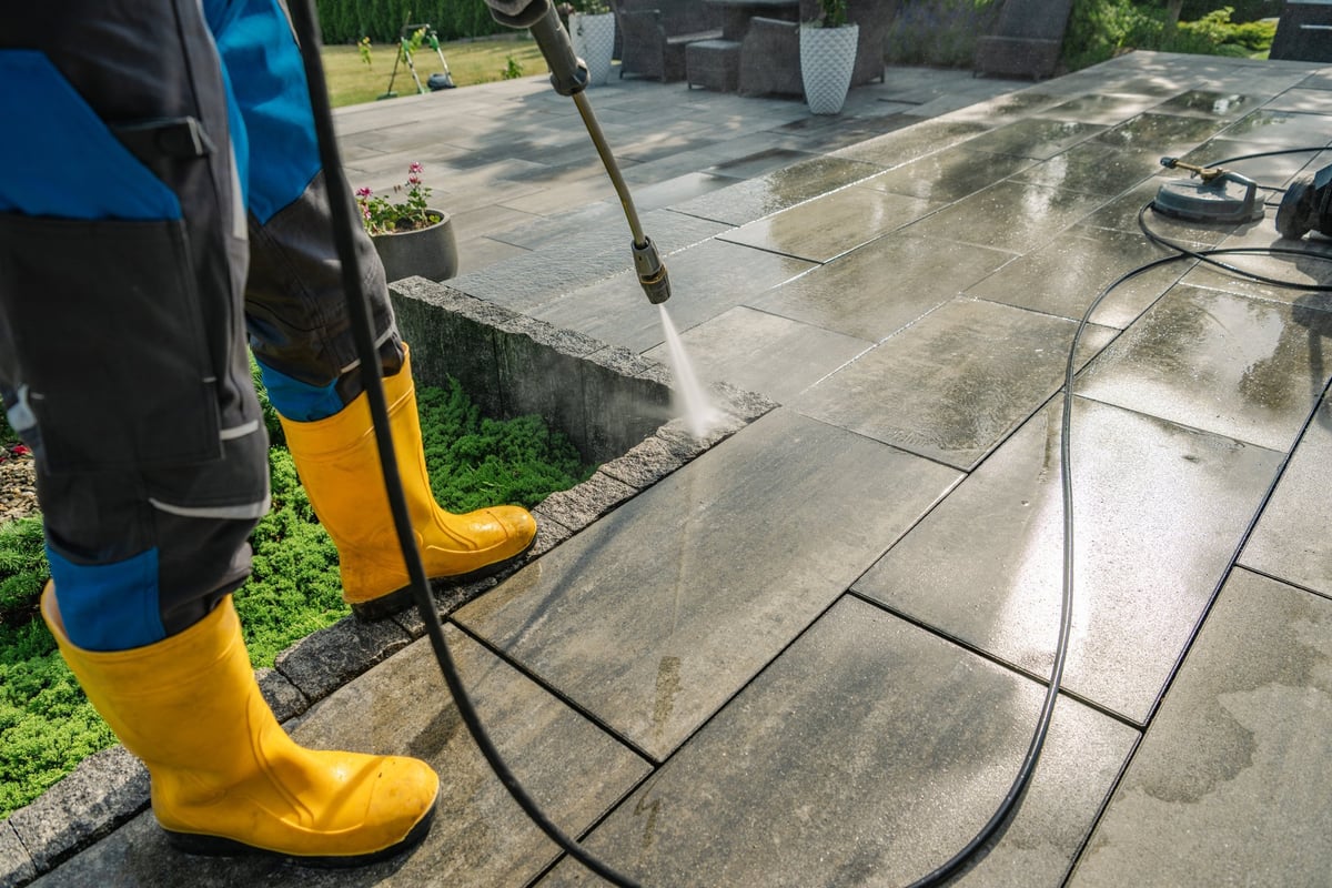 A worker pressure washing a stone patio on a sunny Los Angeles afternoon