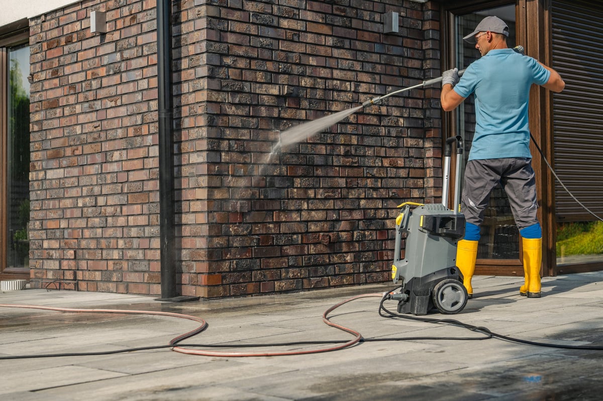 A crew member using a pressure washer to clean the brick wall of a Los Angeles home